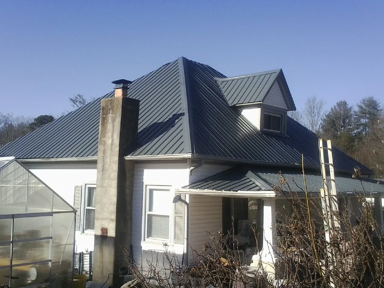 Dark blue standing seam metal roof on a white farmhouse with dormer — Slate & Tile Roof Repair by Roofing Brothers in Big Rapids