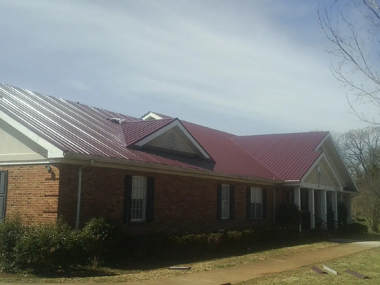 Red metal roof with gabled entries on a long brick building, from a Hail Damage Roof Repair job in Big Rapids
