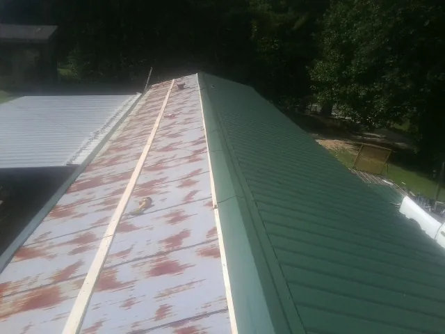 Old rusted panels beside newly installed green metal roofing — Wind Damage Roof Repair by Roofing Brothers in Big Rapids