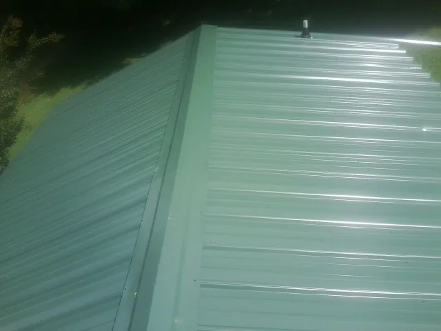 New green metal panels meeting at the ridge of a roof — Flat Roof Repair work by our crew in Big Rapids