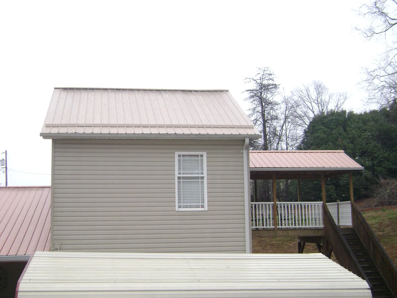 Tan metal roofs on a two story addition and attached porch, from a Roof Replacement job in Big Rapids